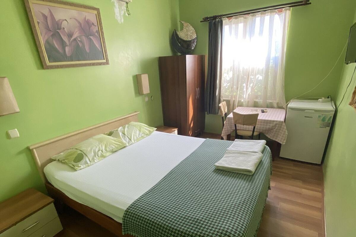 Ein Zimmer mit einem Bett, einem Schreibtisch, einem Stuhl, einem Kühlschrank und einem Fenster mit Vorhängen.