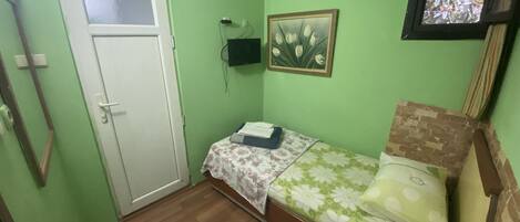 A small, green-walled room with a single bed, a white door, and a small window.