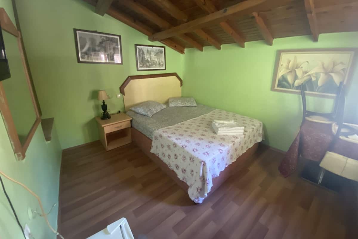 Ein Schlafzimmer mit Holzbalkendecke, einem Bett mit floralem Überwurf, einem Nachttisch mit Lampe und gerahmten Bildern an den Wänden.