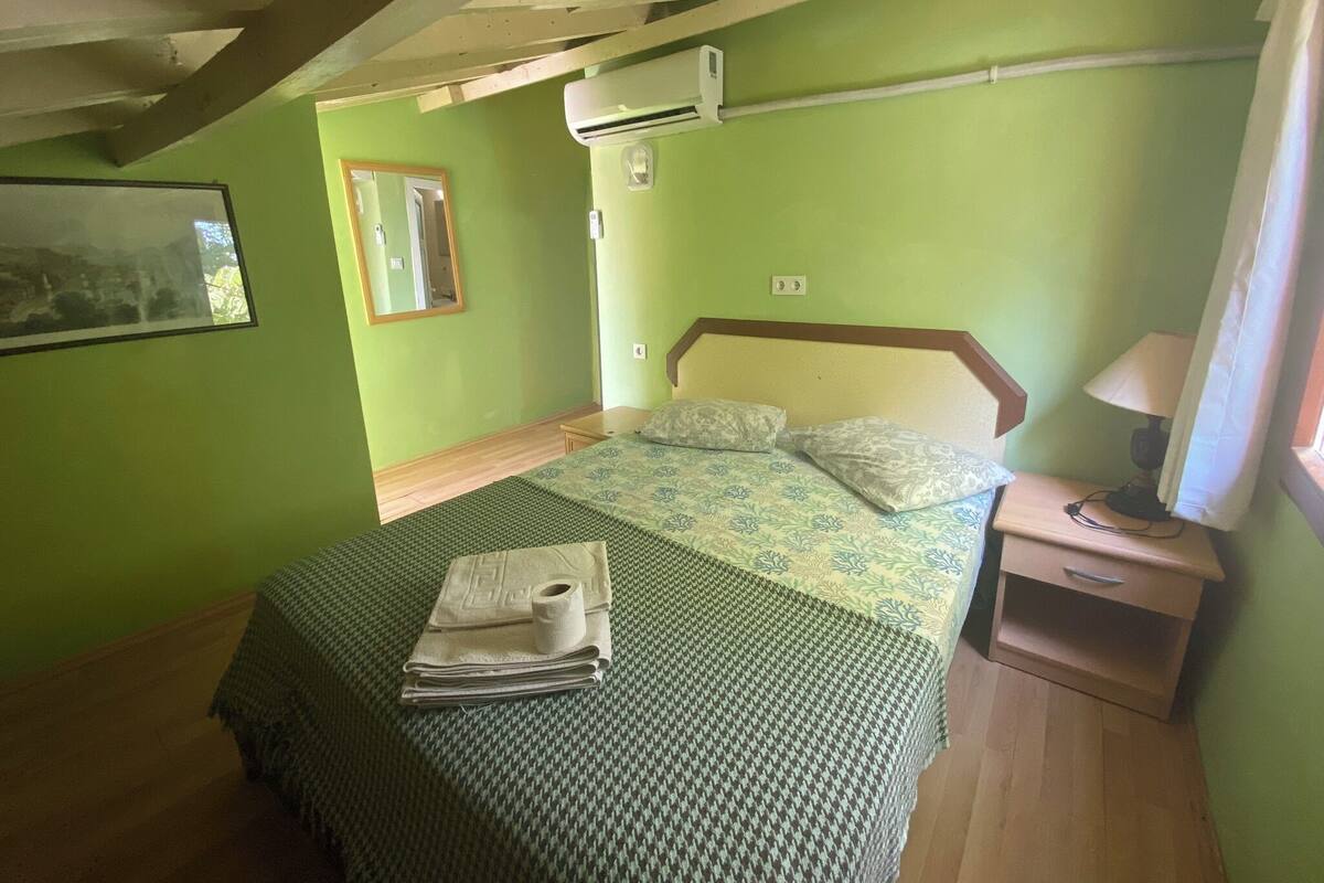 Ein Schlafzimmer mit einem Bett, einem Nachttisch, einer Klimaanlage und einem Fenster mit Vorhängen.