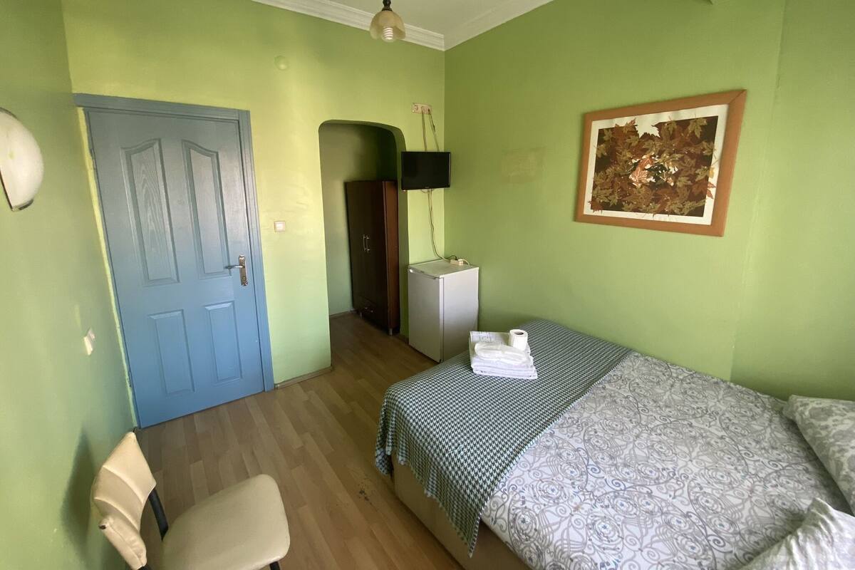 Ein Zimmer mit einem Bett, einem Sessel, einem Schreibtisch, einem Kleiderschrank und einem Gemälde an der Wand.