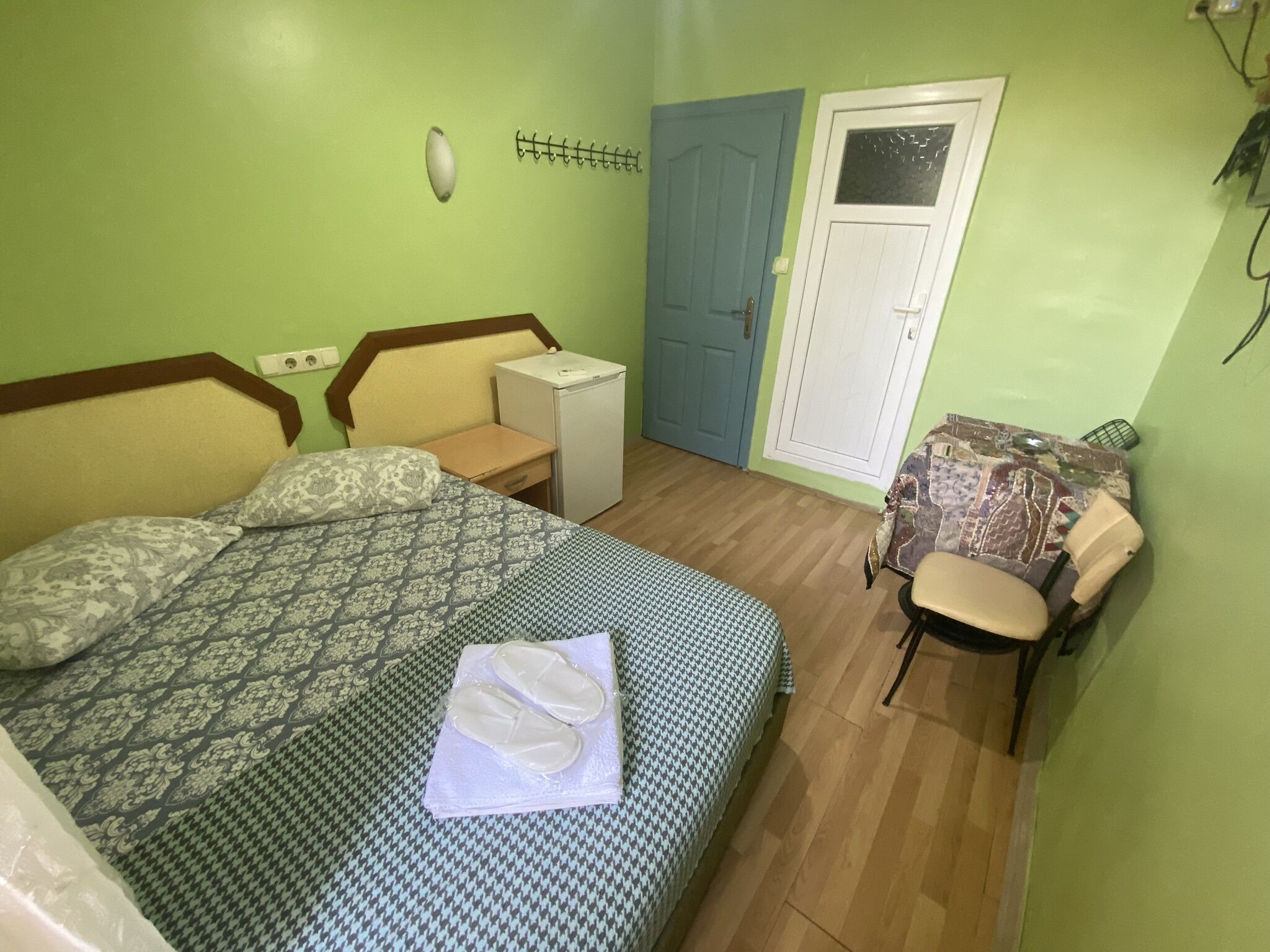 Une chambre à coucher comprenant un lit, une chaise, une petite table, une armoire et un luminaire fixé au mur.