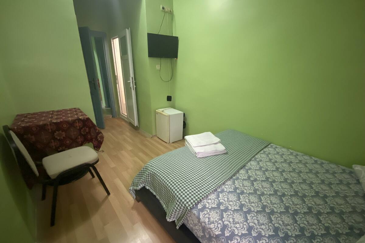 Ein Zimmer mit einem Bett, einem Sessel, einem kleinen Tisch, einem Fernseher und einem Kühlschrank.