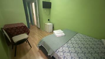 Een kamer met een bed, een stoel, een klein tafeltje, een televisie en een koelkast.