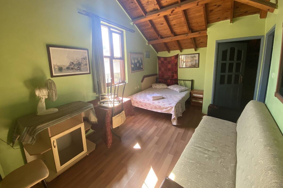 Ein gemütliches Schlafzimmer mit Holzbalkendecke, einem Bett, einem Schreibtisch mit Stuhl und einem Fenster mit Vorhängen.