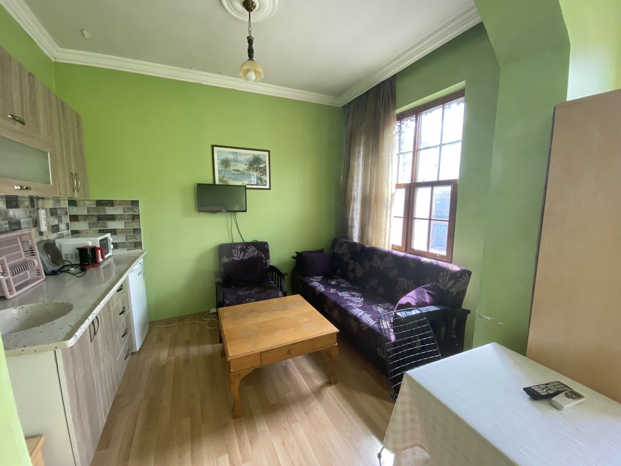 Un espacio habitable compacto con kitchenette, un sofá, una mesa de centro y una ventana con cortinas.