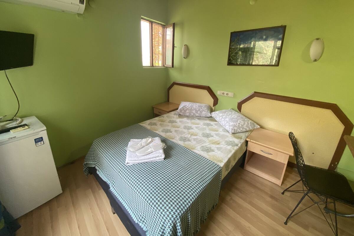 Ein Schlafzimmer mit einem Bett, Nachttischen, einem Sessel, einem Schreibtisch und einem an der Wand befestigten Fernseher.