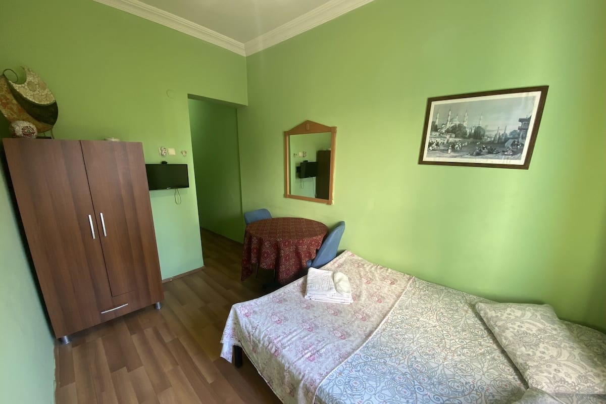 Ein Zimmer mit einem Bett, einem Holzschrank, einem Tisch mit Stühlen, einem Spiegel und einem gerahmten Bild an der Wand.