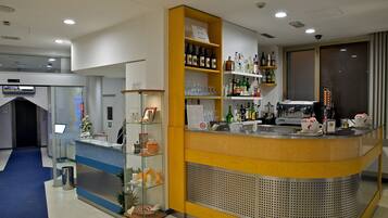 A hotel reception area with a counter, shelves of beverages, a coffee machine, and a glass display case.