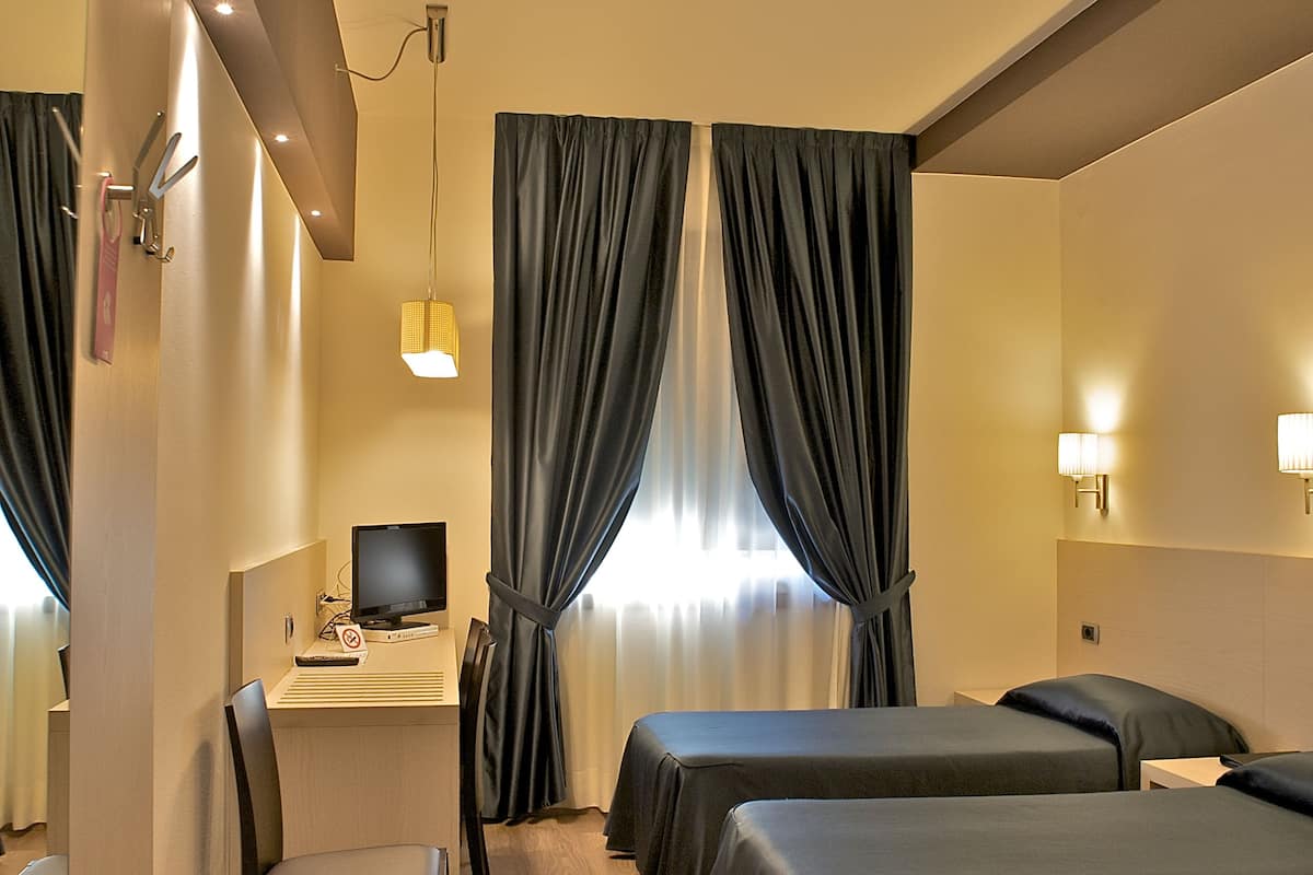 A hotel room with a desk, computer, and three beds.