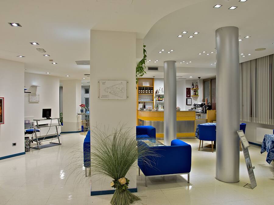 A modern hotel lobby with blue seating, a reception desk, and a bar area.