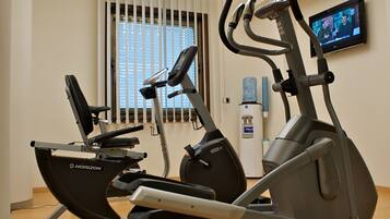 Ein Fitnessraum mit Laufbändern, Ergometer und einem Wasserspender, sowie einem Fernsehbildschirm.