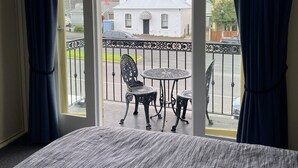 Habitación con balcón que tiene una mesa y sillas, vista a la calle y un edificio al fondo.