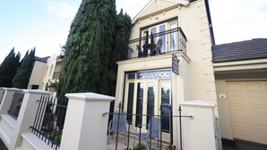 Una casa de dos pisos con balcón, garaje y un árbol alto en el patio.