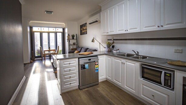 Una cocina moderna con armarios blancos, lavavajillas, microondas y un lavabo.