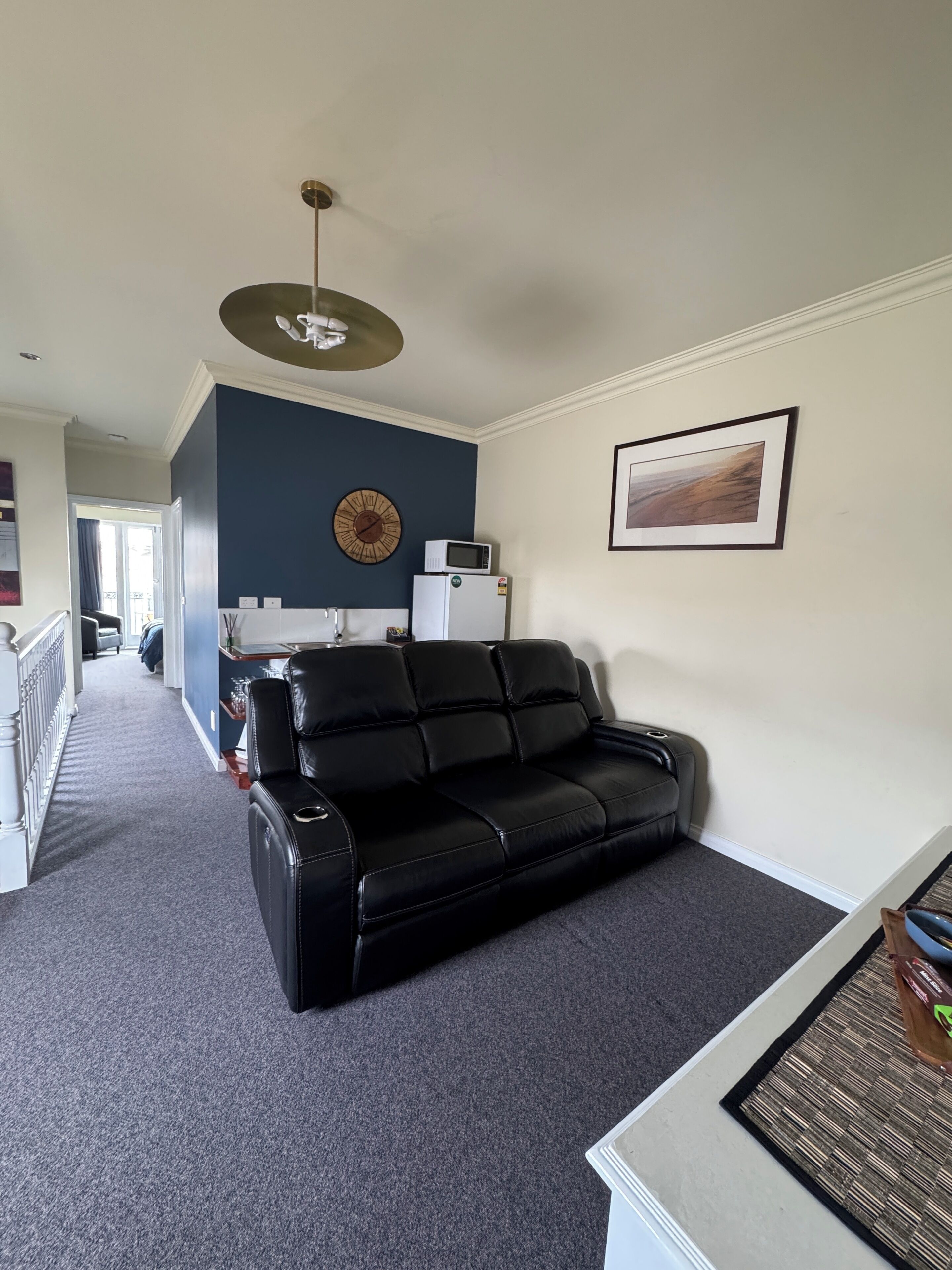 Un salon avec un canapé en cuir noir, un réfrigérateur blanc, une horloge et un tableau encadré accroché au mur.