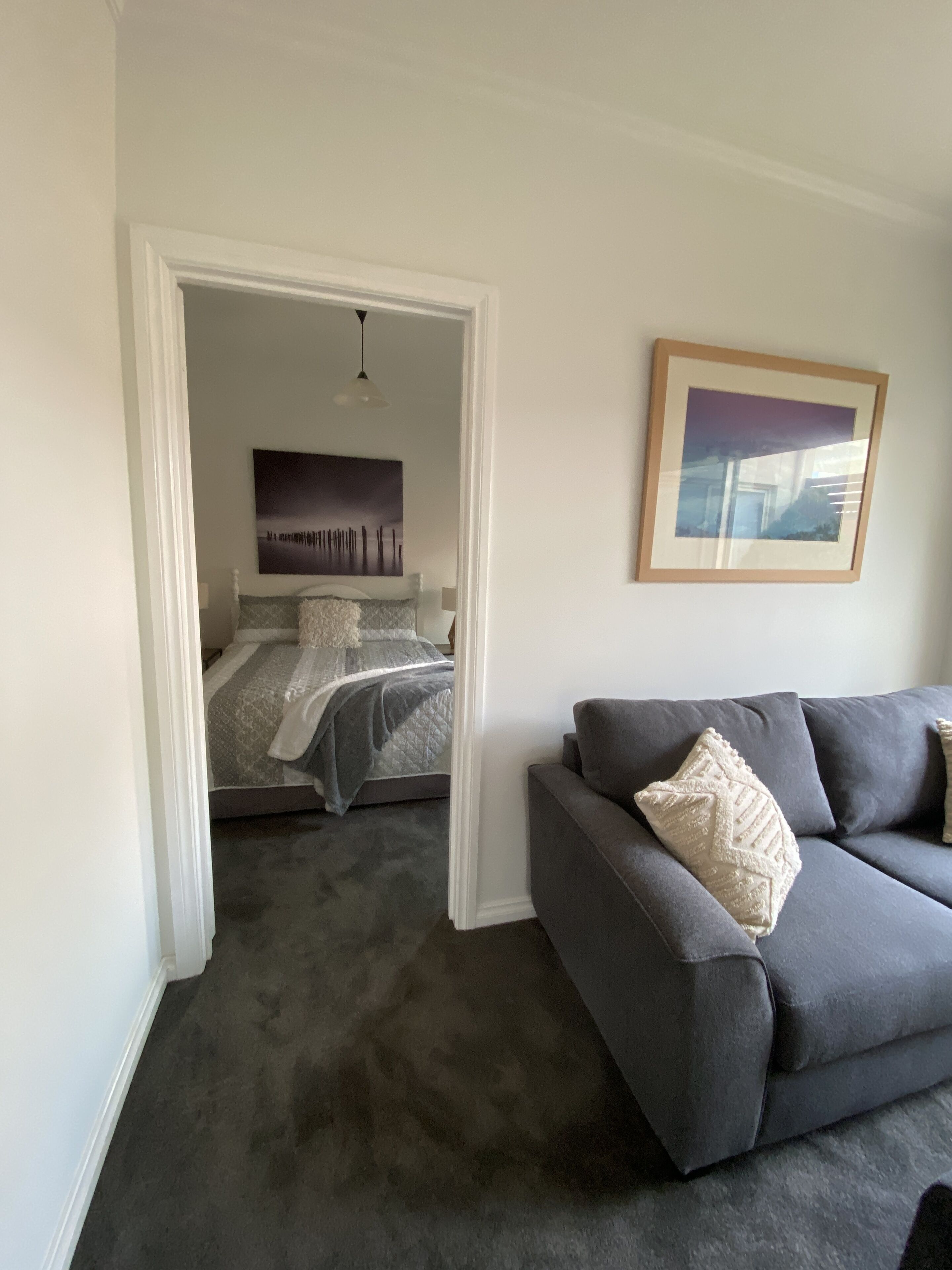 A bedroom with a bed, a grey sofa, and a framed picture on the wall.