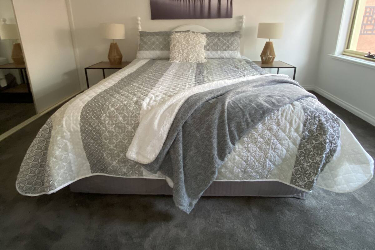 A bedroom with a bed, two bedside tables, a nightstand, a window, and a painting on the wall.