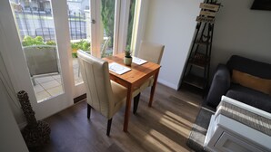 Comedor con mesa y sillas de madera, una planta pequeña en maceta y vistas al exterior a través de un ventanal.