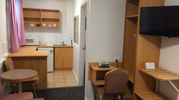 A compact kitchenette with a microwave, sink, and storage shelves. There is a small dining area with a table and two chairs, and a television mounted on the wall.