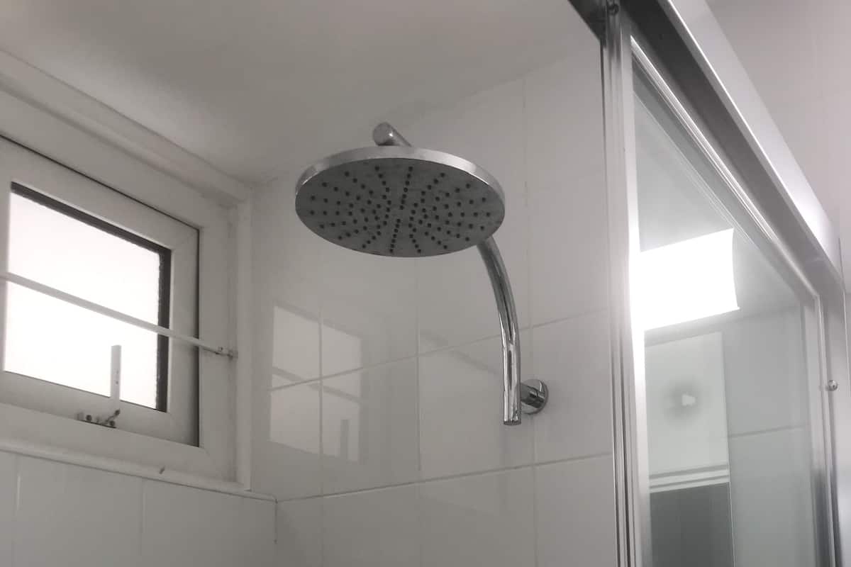 Una ducha con cabezal de ducha de mano, puerta de cristal y una pequeña ventana sobre la ducha.