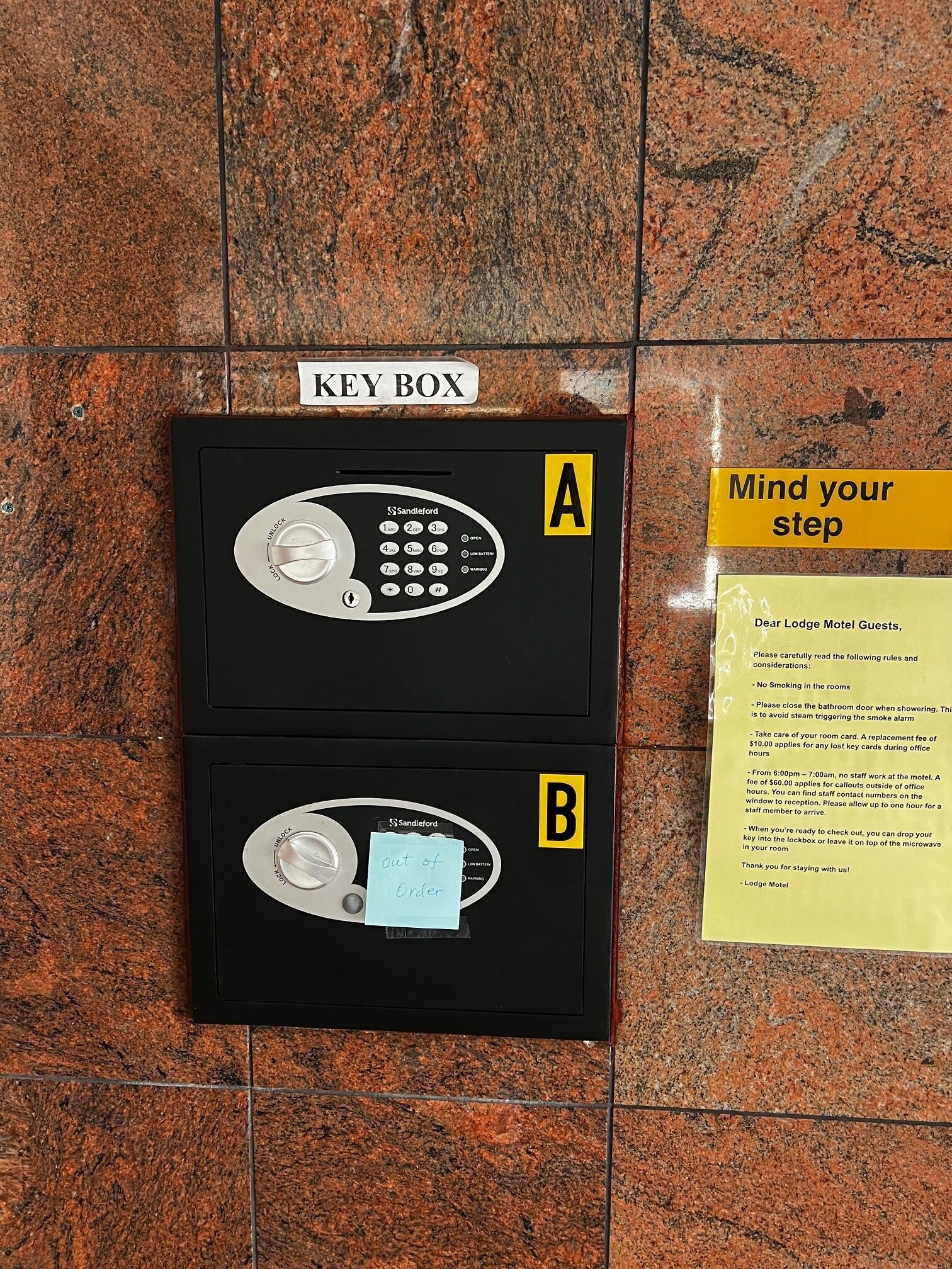 Two key boxes labeled A and B on a tiled floor, with a 'Mind your step' sign nearby.
