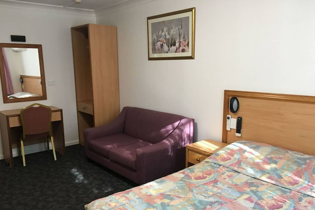Habitación de hotel con cama, escritorio, silla, armario, mesita de noche y un cuadro en la pared.