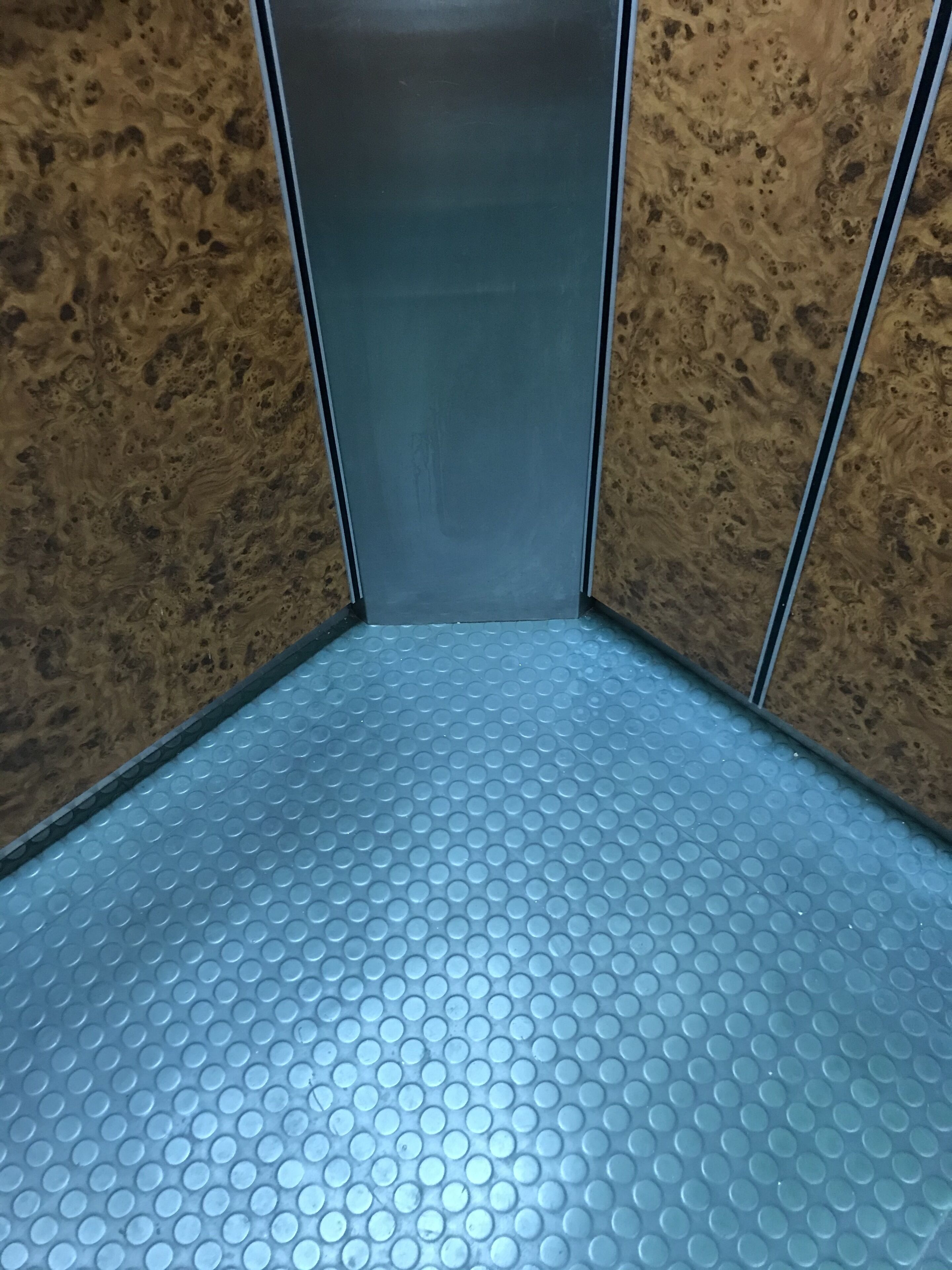 Un ascensore metallico con pavimento a texture e pareti rivestite in legno.