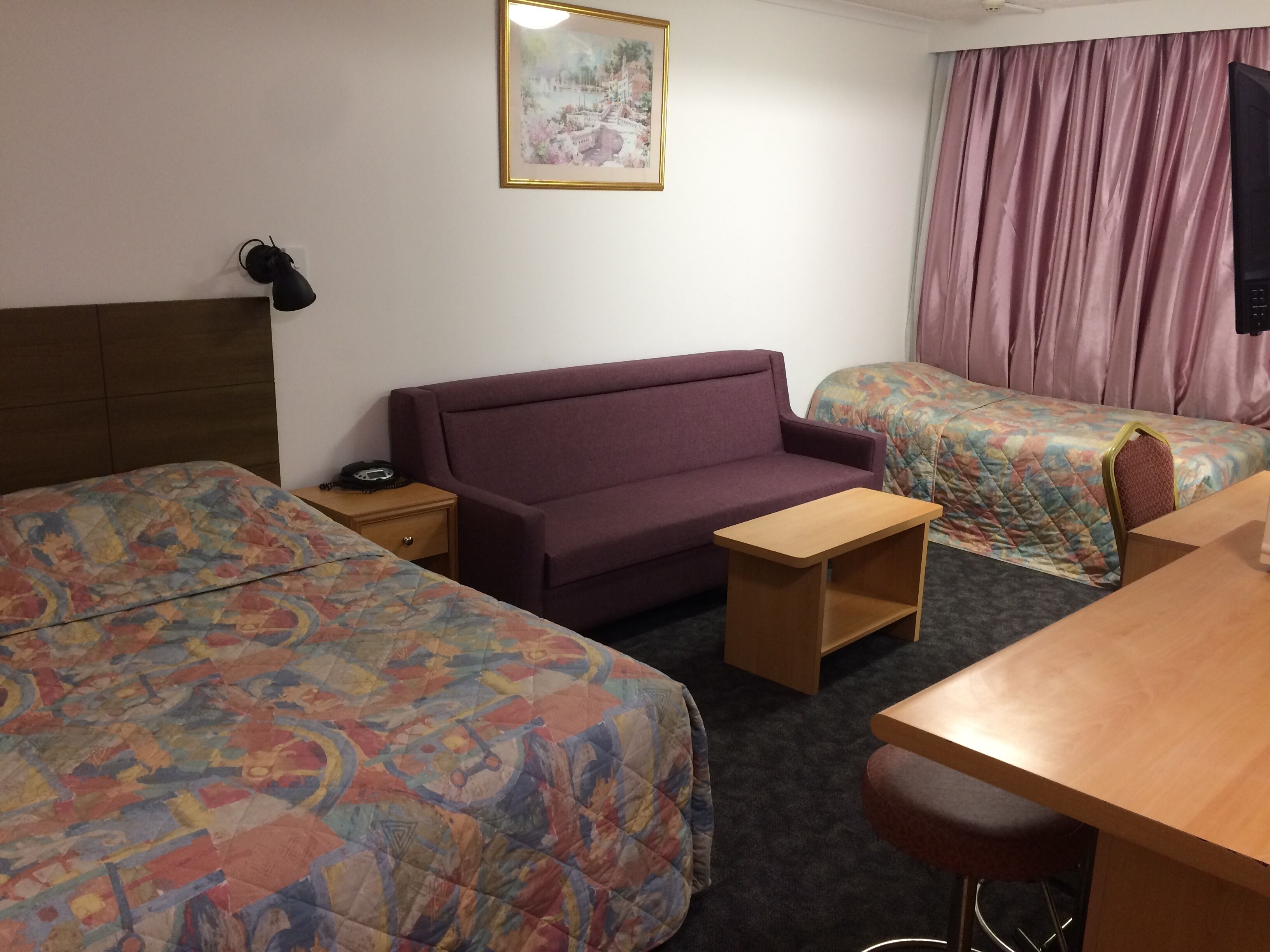 A hotel room with two beds, a sofa, a desk, and a small table.