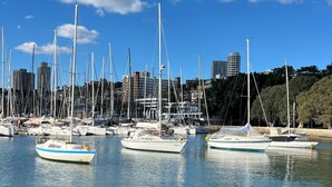 A marina with multiple sailboats docked, a city skyline in the background, and calm water.