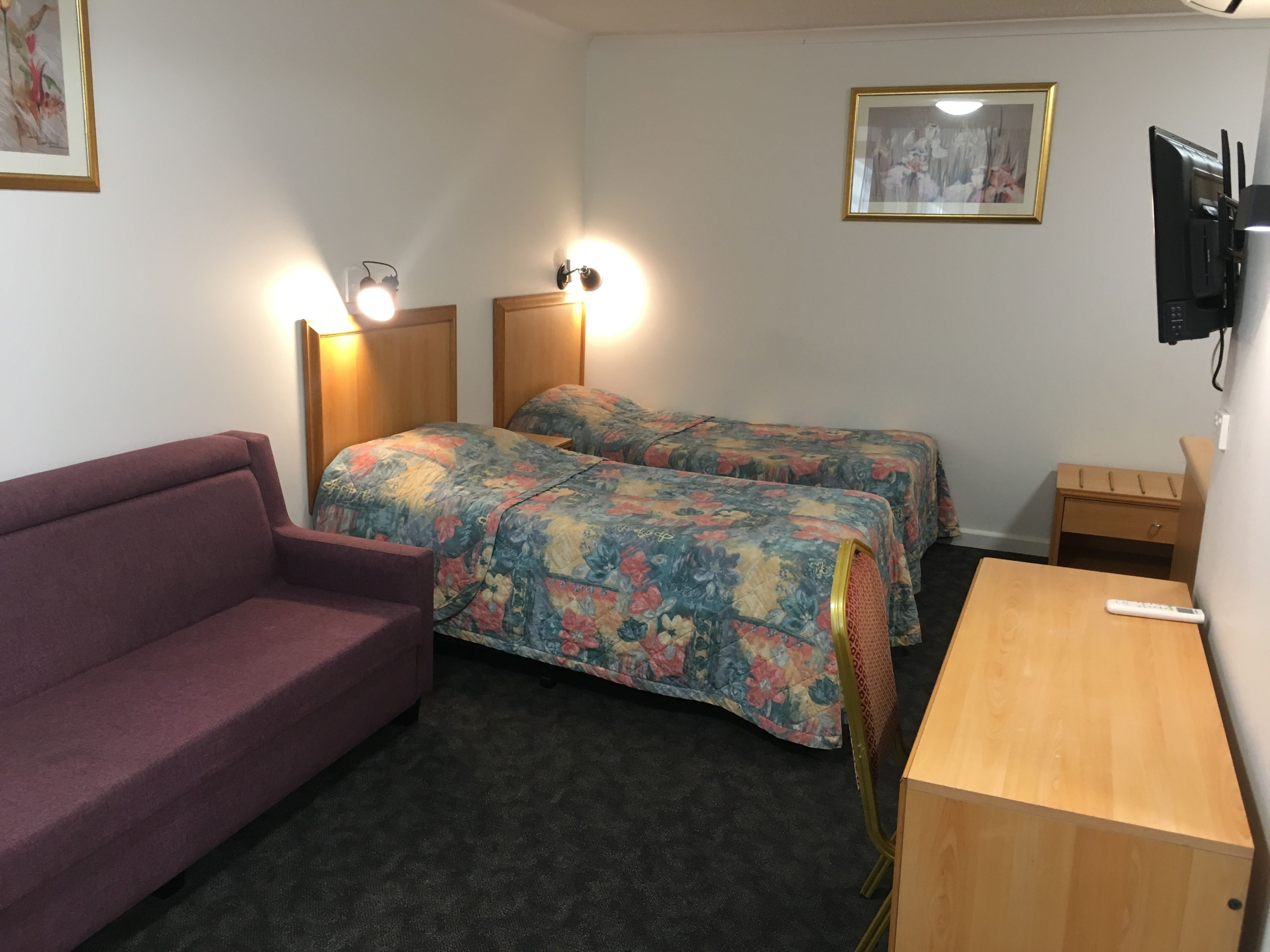 A room with two beds, a couch, a wooden desk, and a TV mounted on the wall.