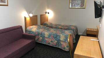 A room with two beds, a couch, a wooden desk, and a TV mounted on the wall.