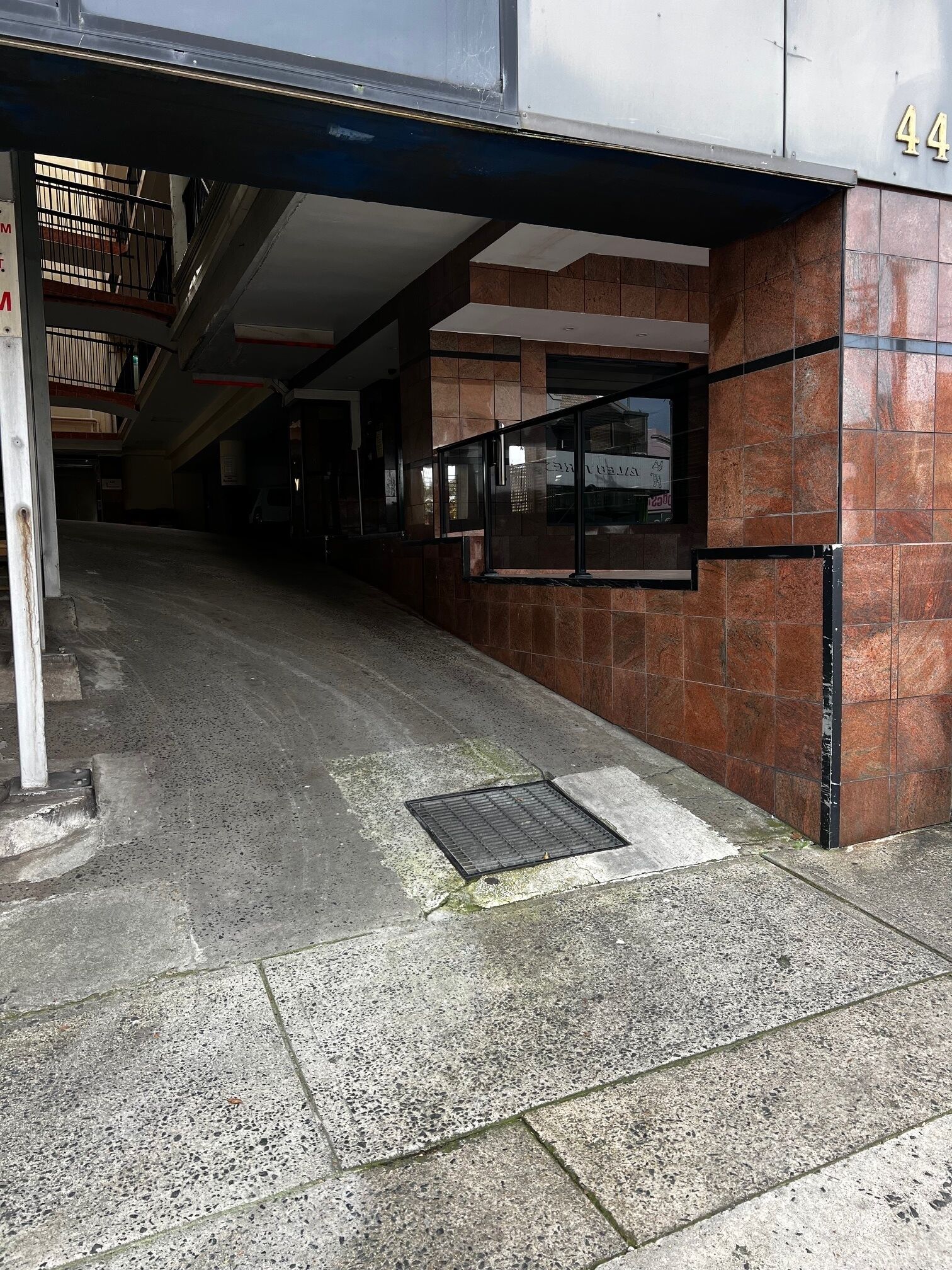 Entrada de un edificio con un muro de azulejos, un marco de puerta metálico y el número 44 a la vista.