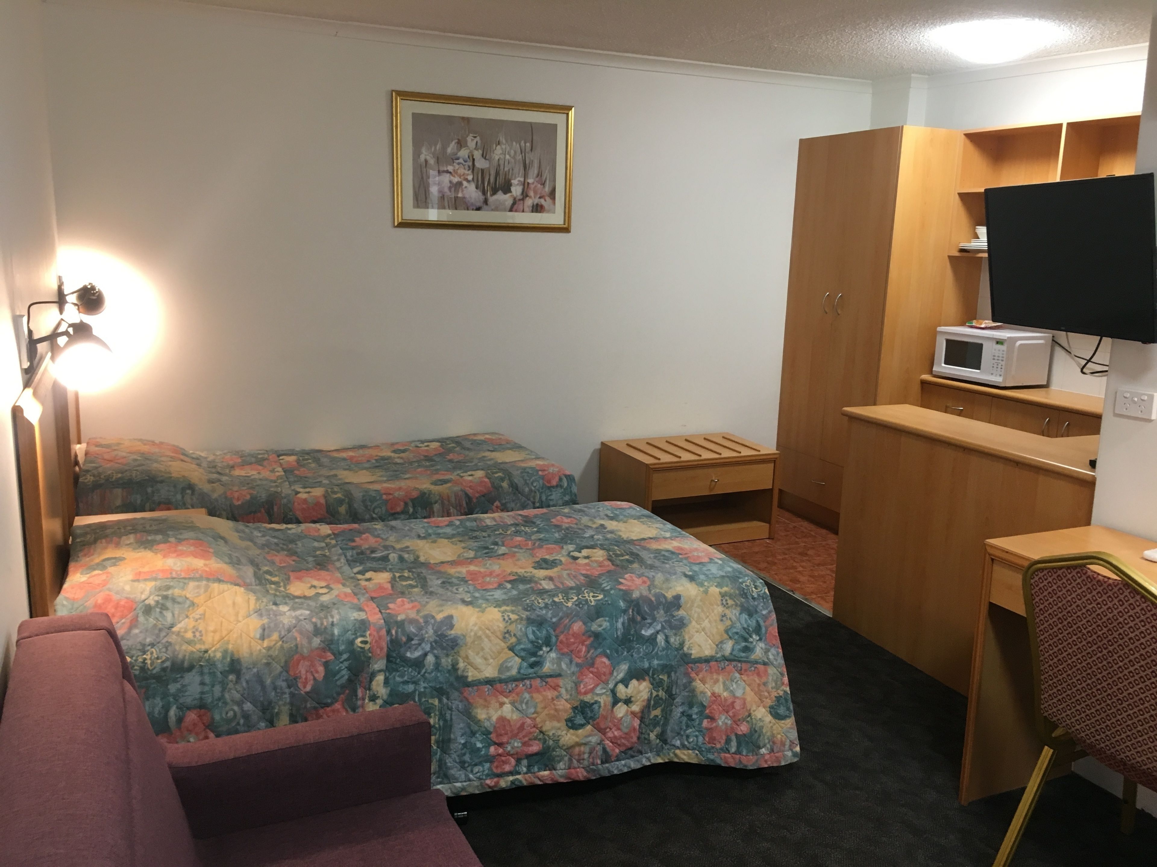 A hotel room with two beds, a desk, a chair, a television, and a microwave.