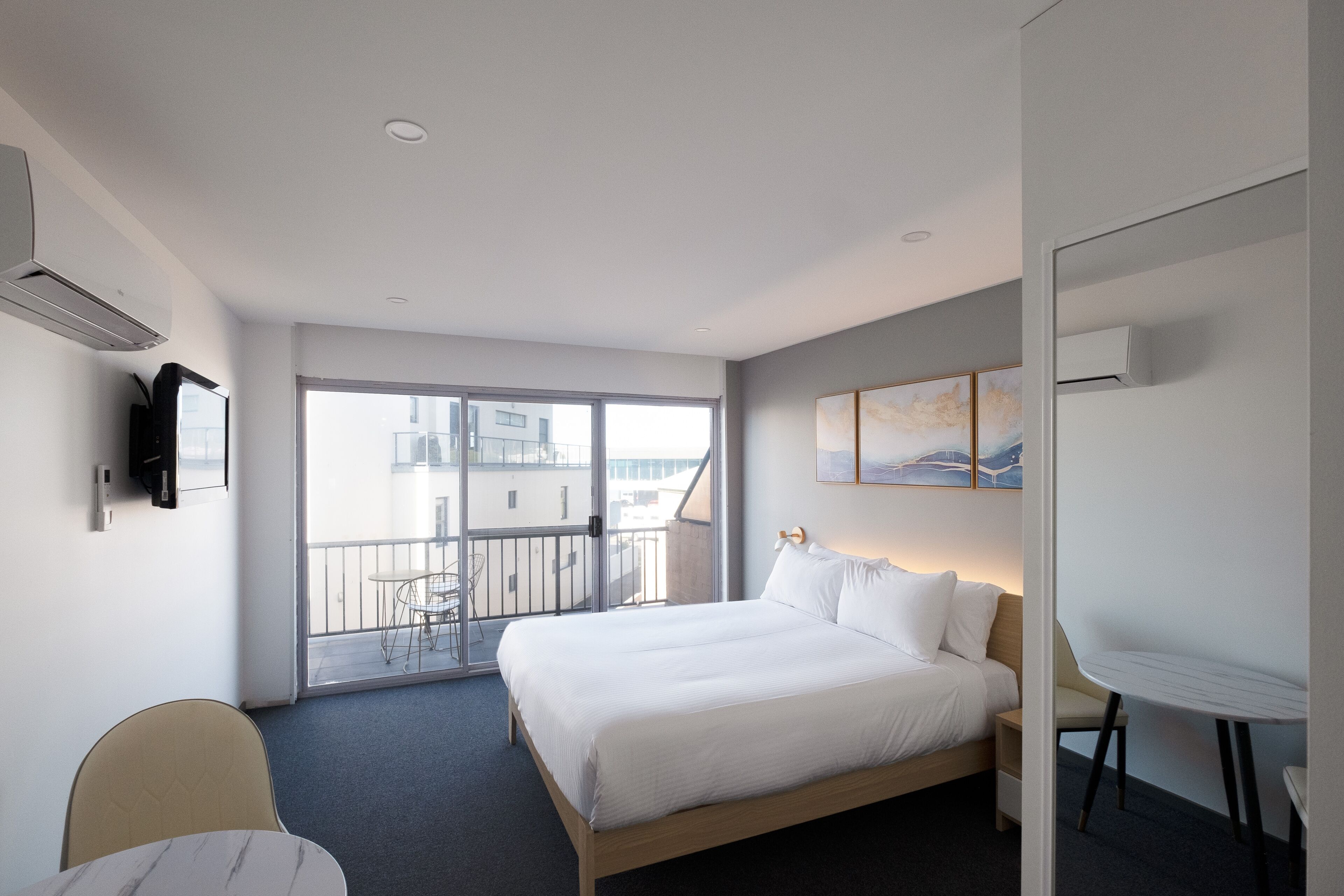 A modern hotel room with a large bed, a desk, and a balcony with a view of the city.
