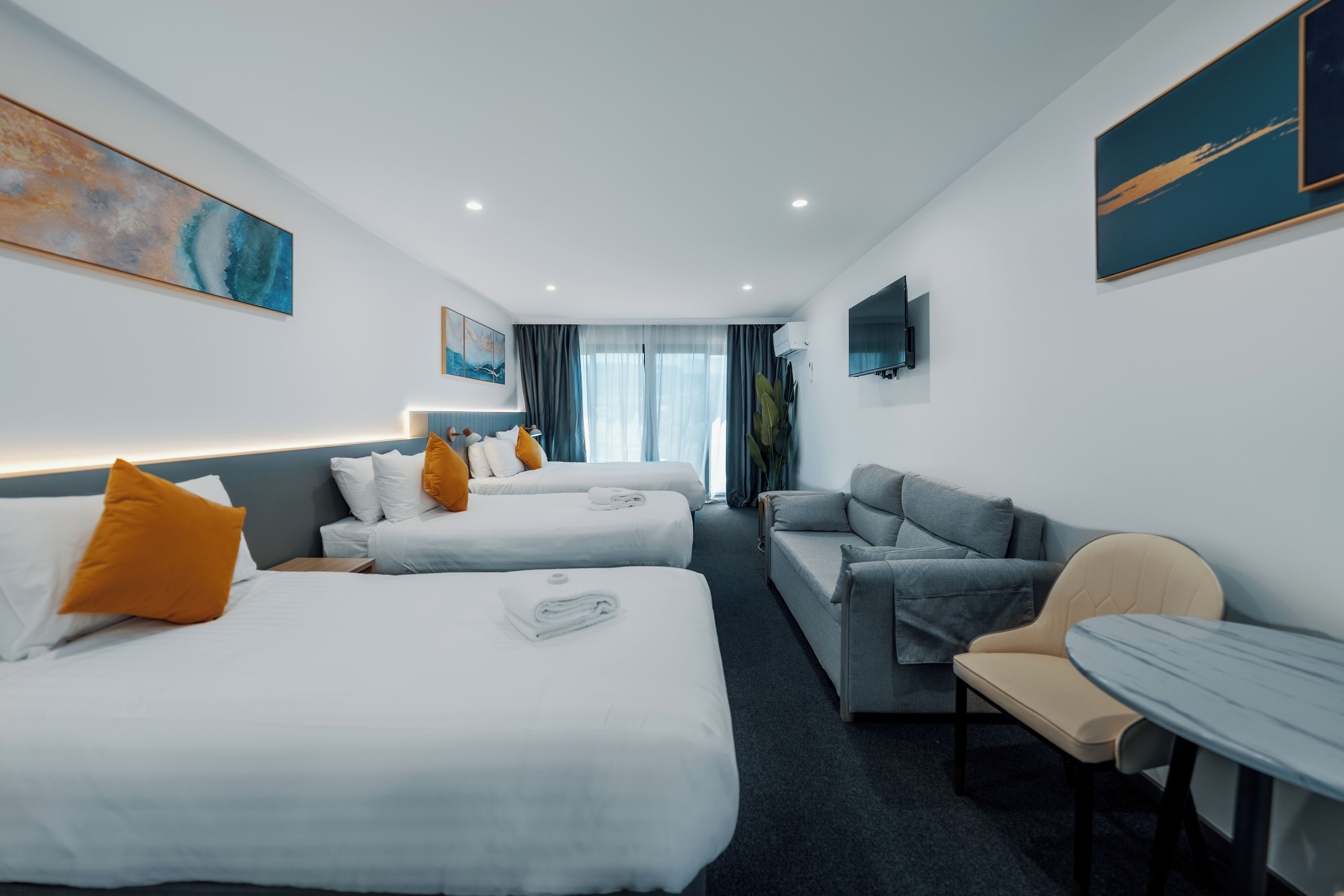 A hotel room with two beds, a sofa, a table, and a TV.
