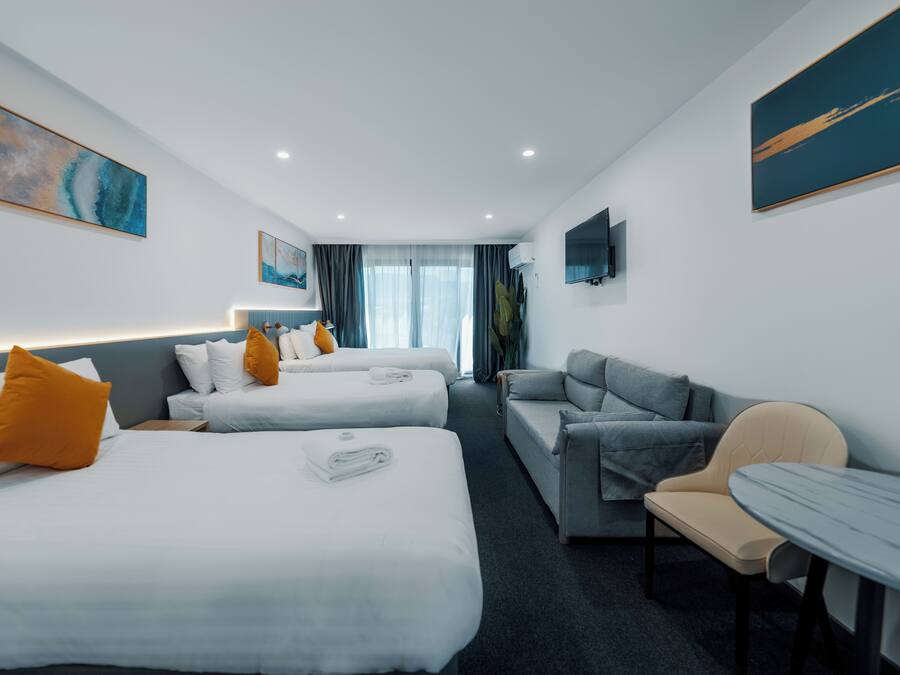 A hotel room with two beds, a sofa, a table, and a TV.