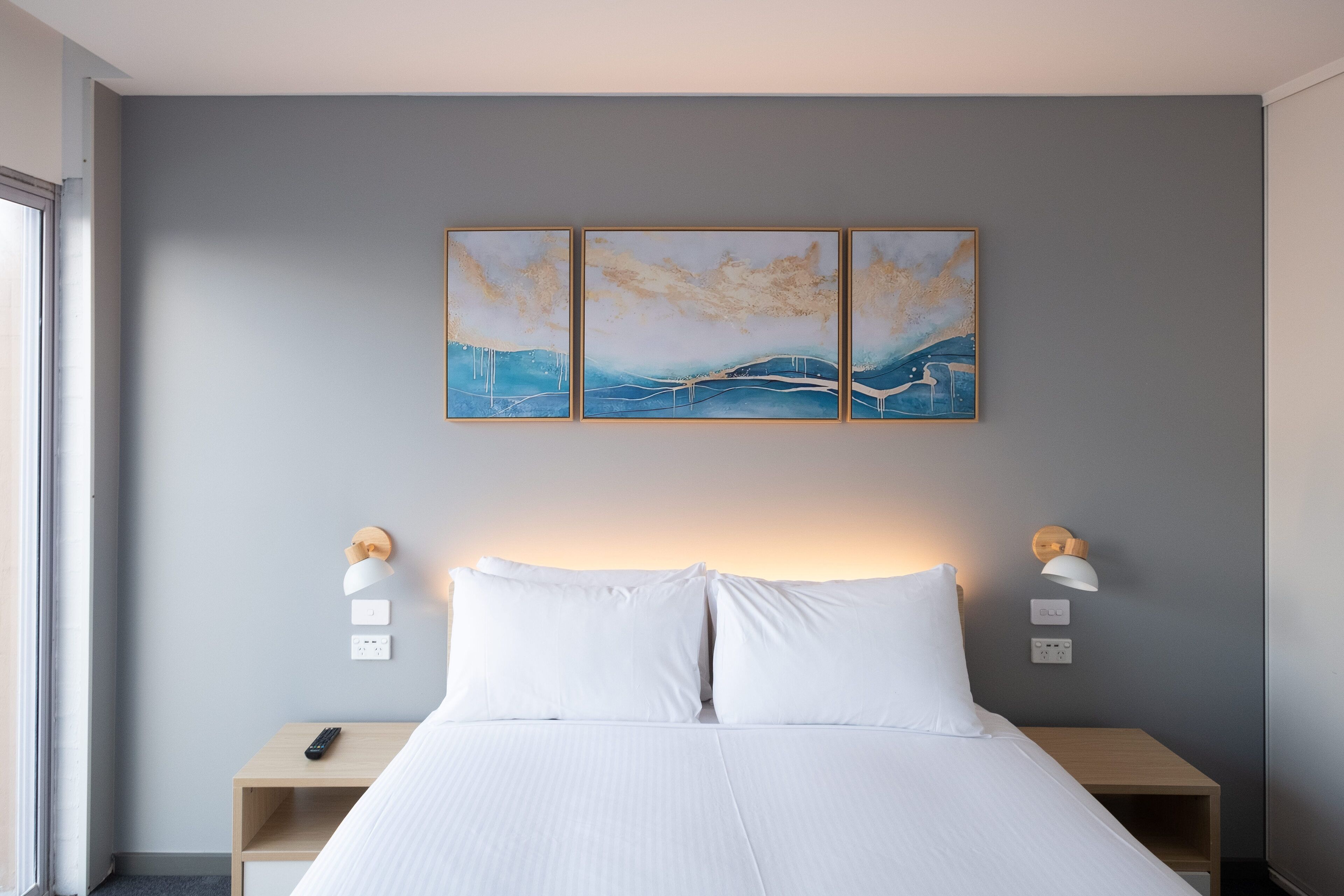 Une chambre d’hôtel avec un lit, des tables de chevet, des lampes fixées au mur et un tableau au-dessus du lit.