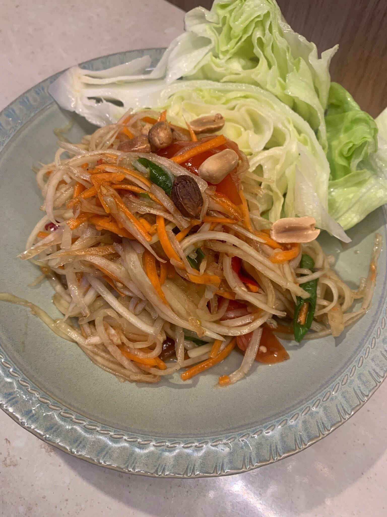A plate of stir-fried noodles with vegetables and peanuts, served with a side of lettuce.