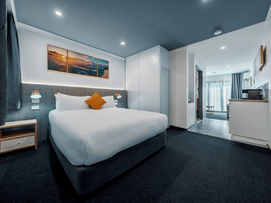 A modern hotel room with a large bed, bedside tables, a desk, and a view of the city.