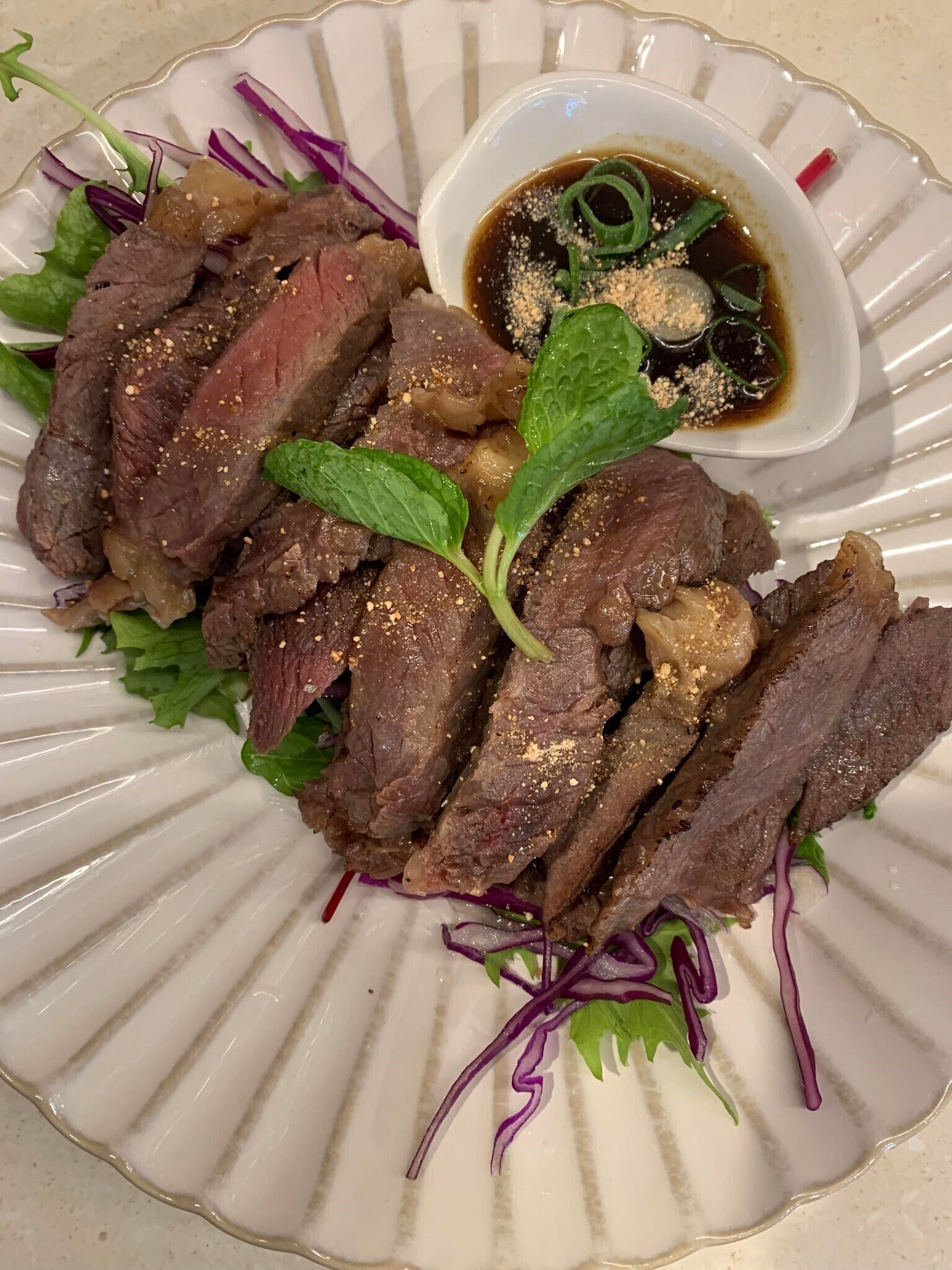 Un plato de carne de res en rodajas adornado con hierbas y un tazón pequeño de salsa.