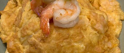 A plate with an omelette, shrimp, and a small bowl of sauce.