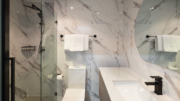 A modern bathroom with a glass-enclosed shower, a white toilet, and a large mirror above a white sink with a black faucet.