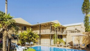 A swimming pool with lounge chairs and palm trees, surrounded by a building with balconies.