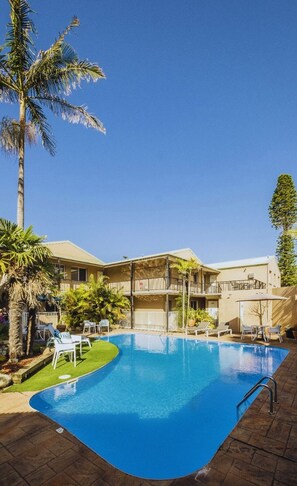 A swimming pool with lounge chairs, palm trees, and a building with balconies.