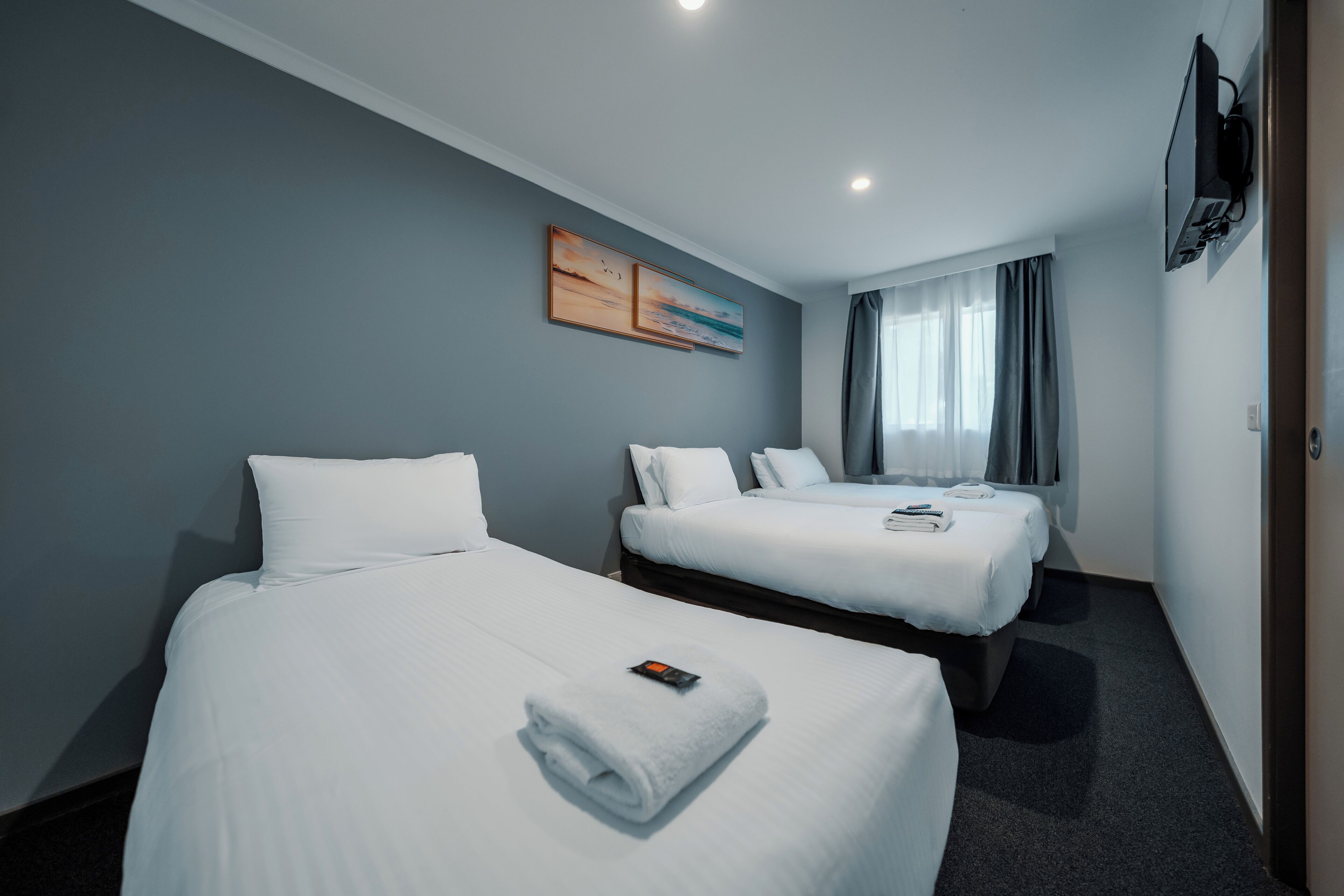 A hotel room with two beds, a flat-screen TV mounted on the wall, and a painting above the beds.