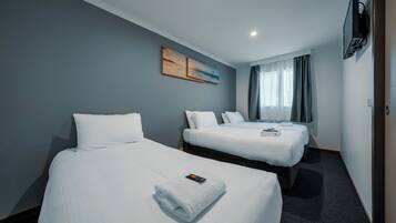 A hotel room with two beds, a flat-screen TV mounted on the wall, and a painting above the beds.