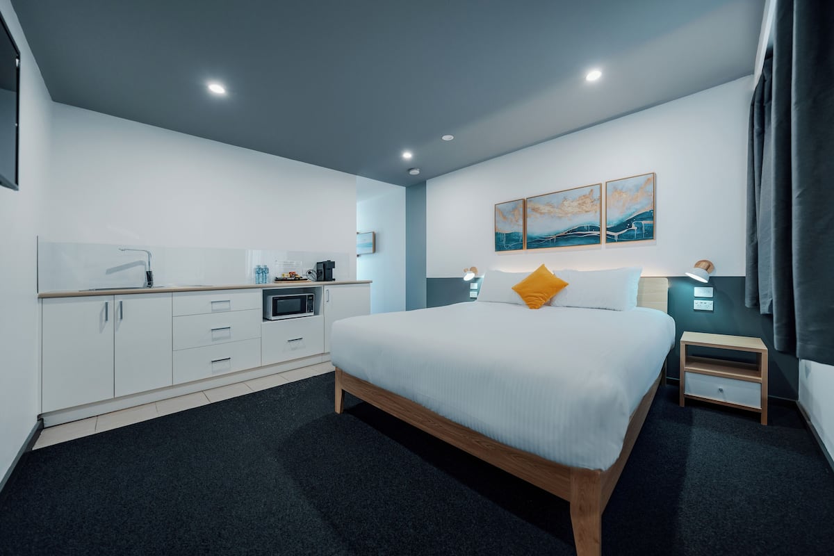 A modern hotel room with a large bed, a desk, a microwave, and a small cabinet.