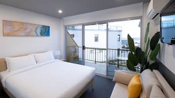 Habitación de hotel moderna con una cama grande, un sofá, un balcón con vistas y un cuadro en la pared.