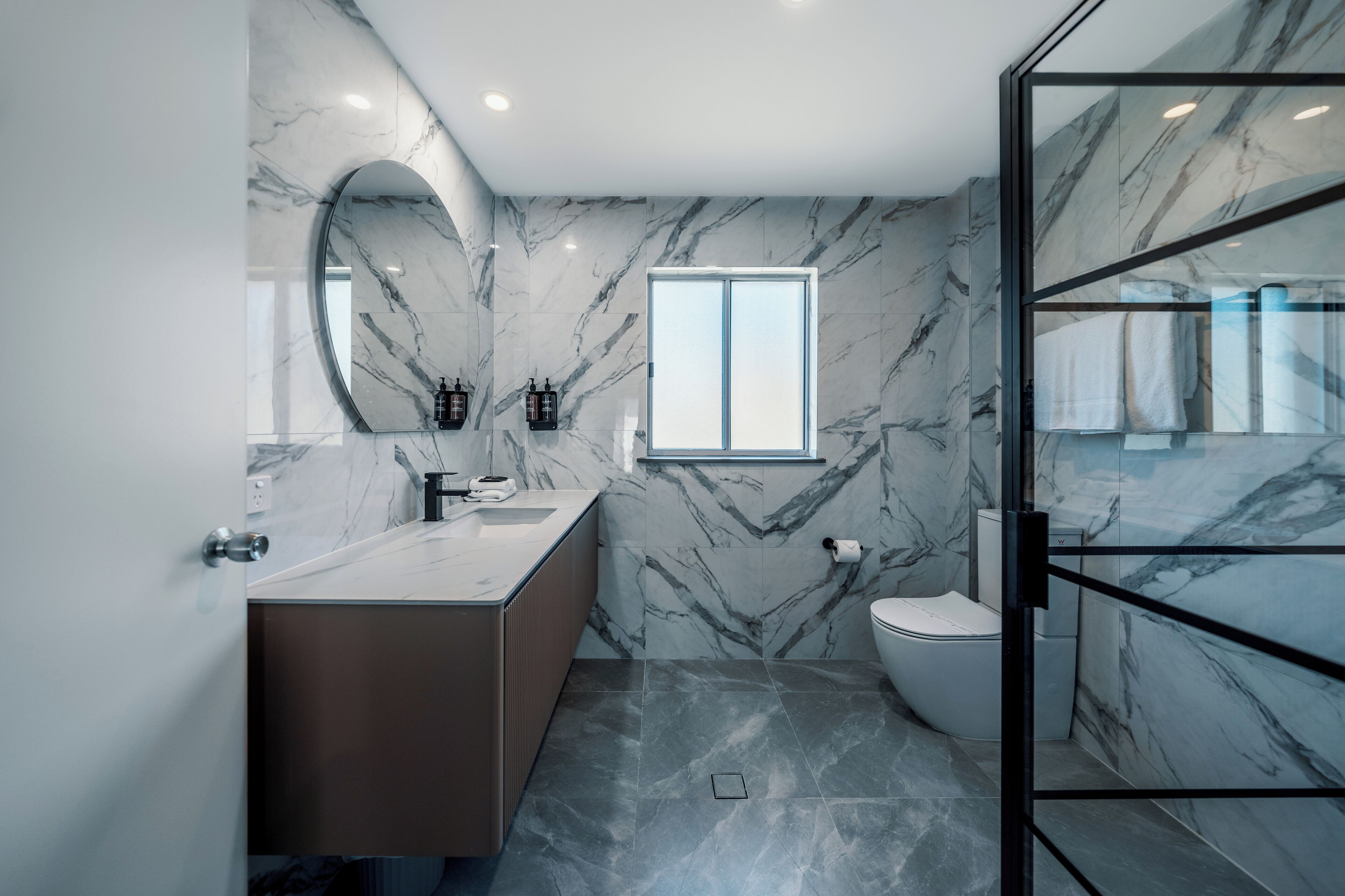 A modern bathroom with marble walls, a glass shower enclosure, and a large mirror.